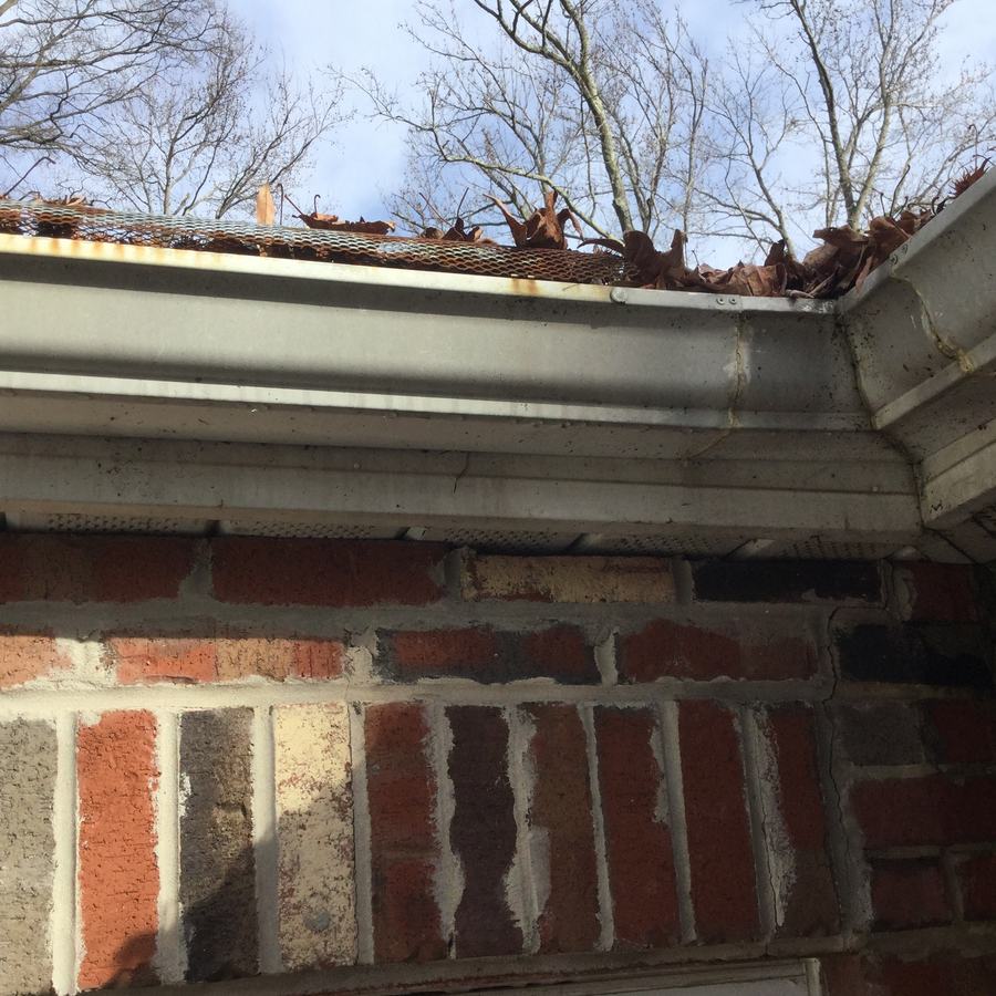 An older screen gutter guard with leaves sitting on top of it and coming out of the gutter