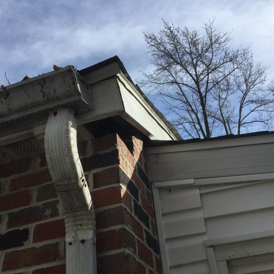 Dirty gutter with debris sticking out of the top and streaks down its face